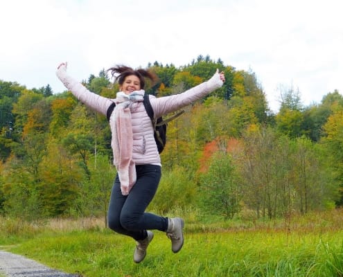 Frau im Wald, die in die Luft springt; Symbolbild für Freude