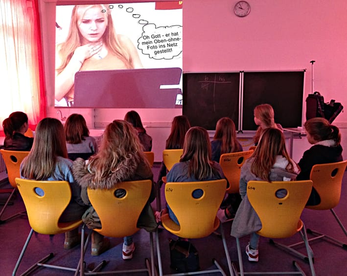 Klassenzimmer mit Schülerinnen, die sich ein projiziertes Bild anschauen