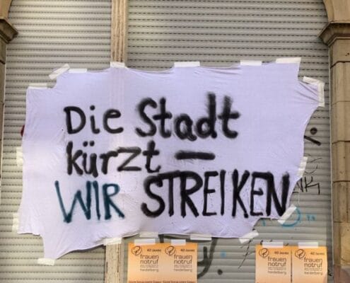 Tuch außen an der Fassade des Frauennotruf mit den Worten: Die Stadt kürzt - WIR STREIKEN