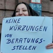 Frau hält Schild mit der Aufschrift "Keine Kürzungen von Beratungsstellen"